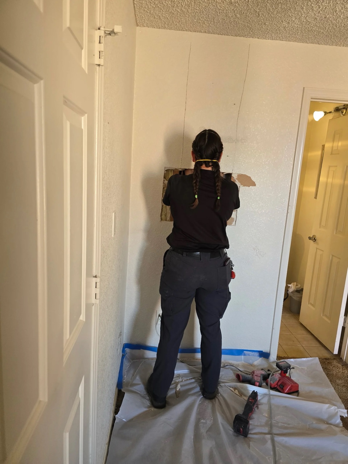 Western Sky Plumbing technician opening a small drywall access to reach a hidden water leak in Phoenix